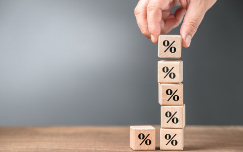 Closeup hand stack up the wood cubes with percentage symbol, mathematics, commission, or compound interest concept