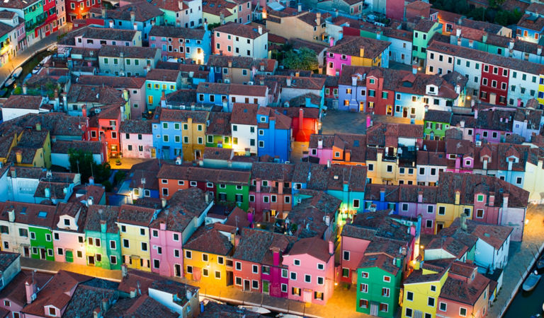 As the evening sets in, the colorfully painted house facades of Burano Island come alive in a warm, glowing ambiance. Situated in the province of Venice, Italy, this charming island is renowned for its vibrant architecture. This photograph captures the un