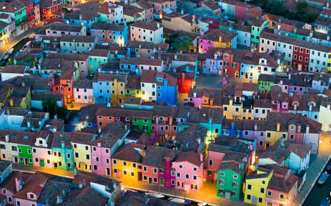 As the evening sets in, the colorfully painted house facades of Burano Island come alive in a warm, glowing ambiance. Situated in the province of Venice, Italy, this charming island is renowned for its vibrant architecture. This photograph captures the un