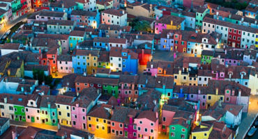 As the evening sets in, the colorfully painted house facades of Burano Island come alive in a warm, glowing ambiance. Situated in the province of Venice, Italy, this charming island is renowned for its vibrant architecture. This photograph captures the un
